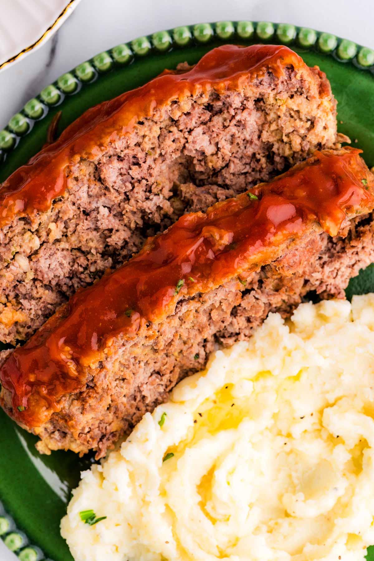 Close up of meatloaf on plate with mashed potatoes.