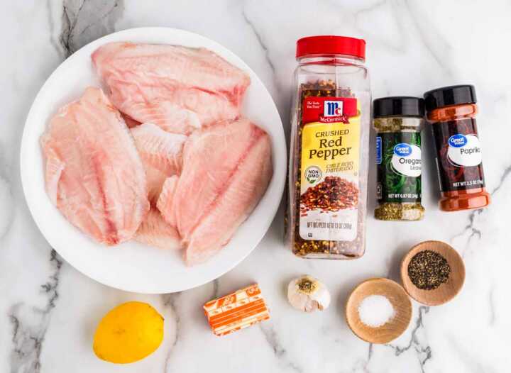 Ingredients for baked tilapia on white marble surface.