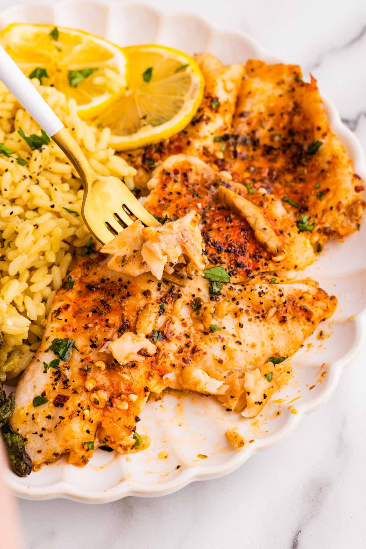 Baked tilapia served on a white plate with yellow rice.