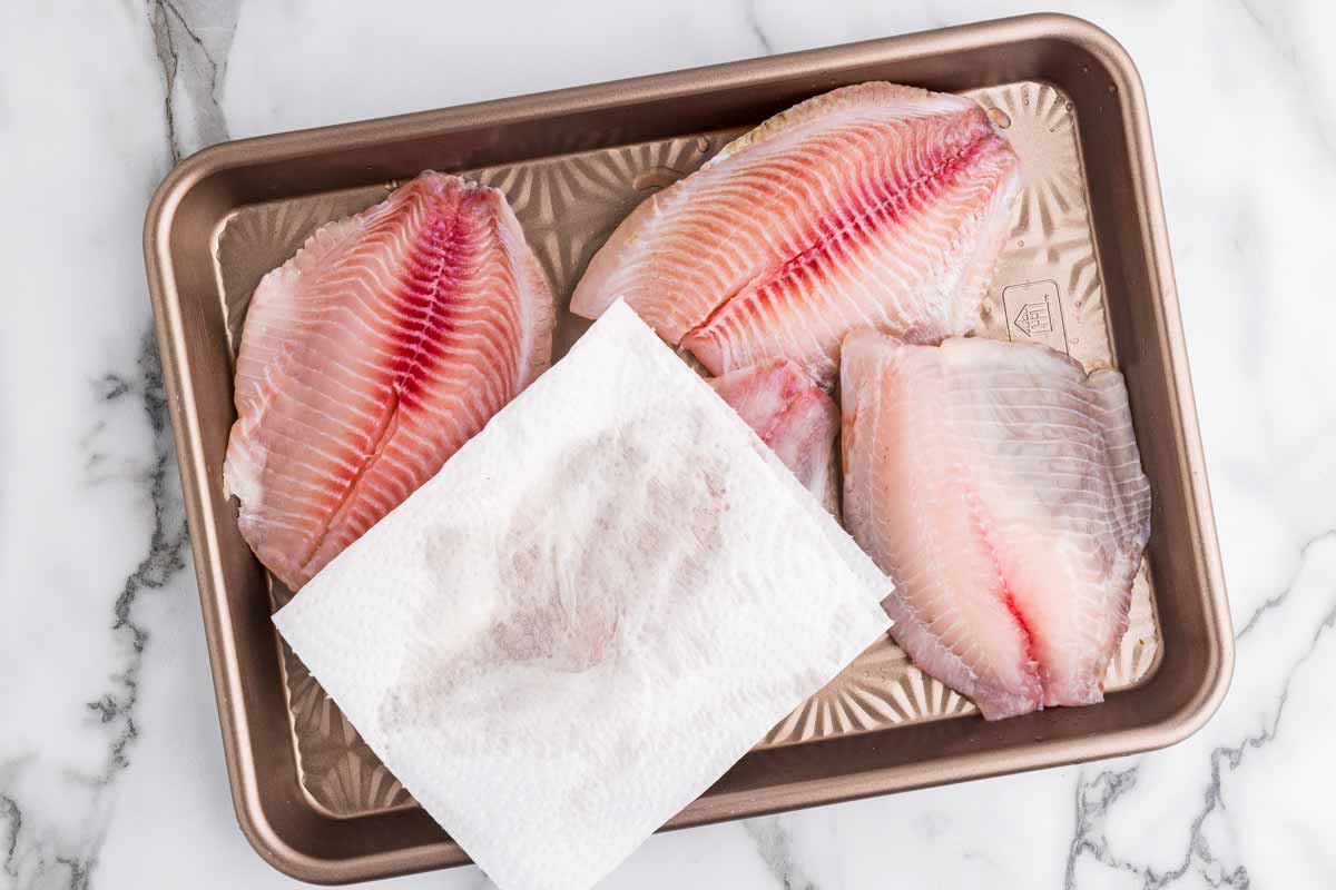 Patting dry tilapia with paper towels.