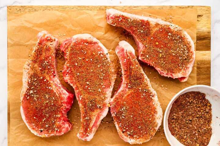 Pork chops on a wooden cutting board, seasoned with spice rub.