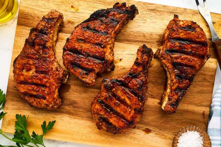 Grilled pork chops resting on a wooden cutting board.