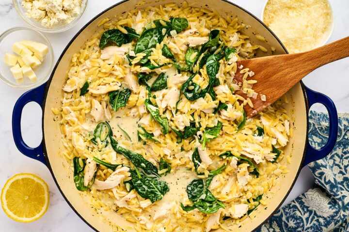 Stirring spinach, chicken and cream into orzo in a pan.