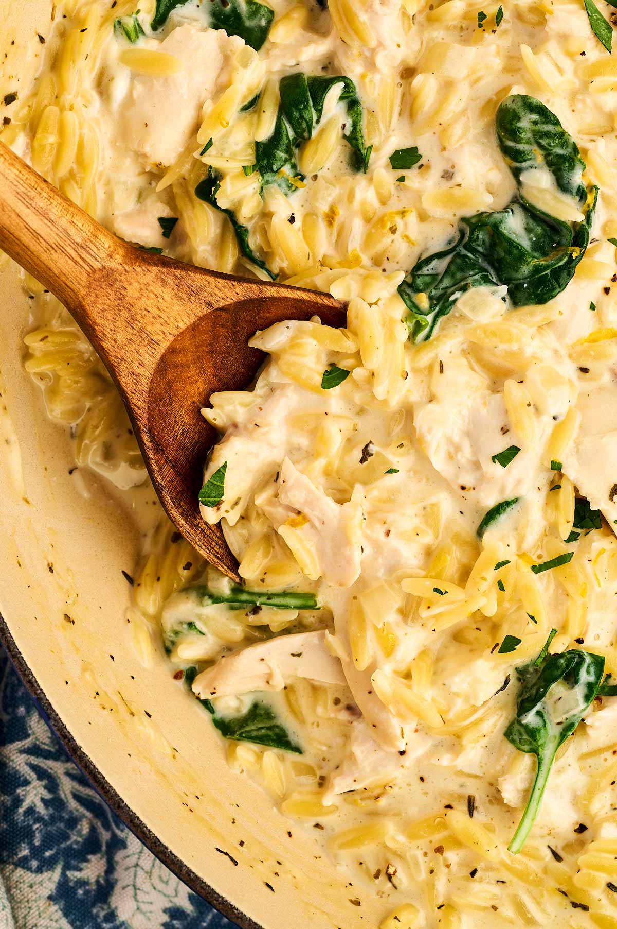 Overhead view of wooden spoon stuck in a pan with lemon chicken orzo pasta.
