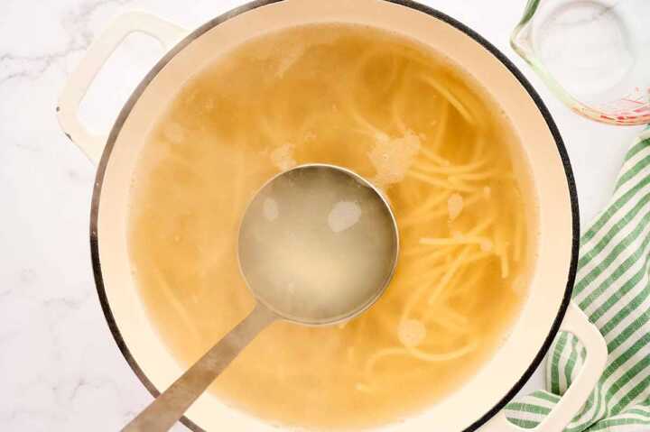 Scooping pasta cooking water from a pot of spaghetti.