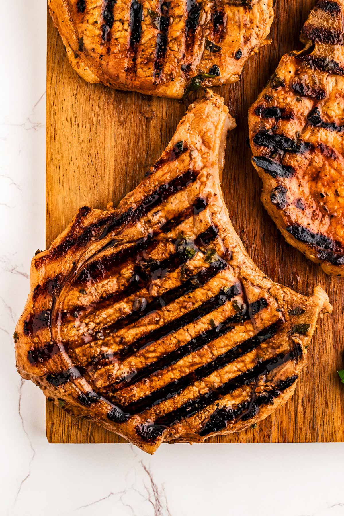 Marinated grilled pork chops on a wooden cutting board.