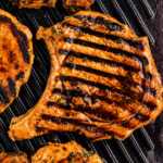 Grilled marinated pork chops on grill grates.