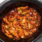 Black slow cooker crock filled with honey garlic chicken.