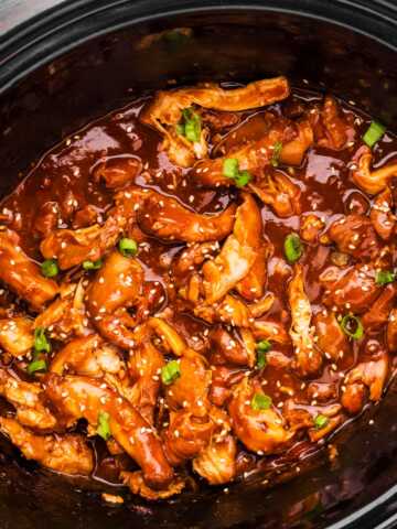 Black slow cooker crock filled with honey garlic chicken.