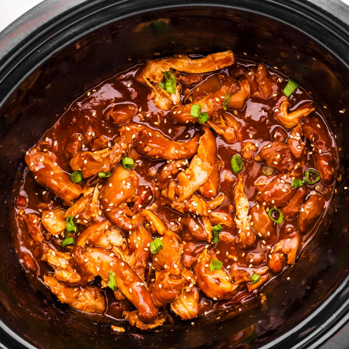 Black slow cooker crock filled with honey garlic chicken.