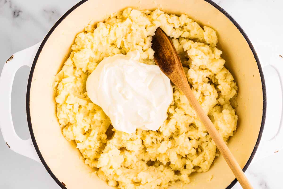 Sour cream dolloped on mashed potatoes in a pot.
