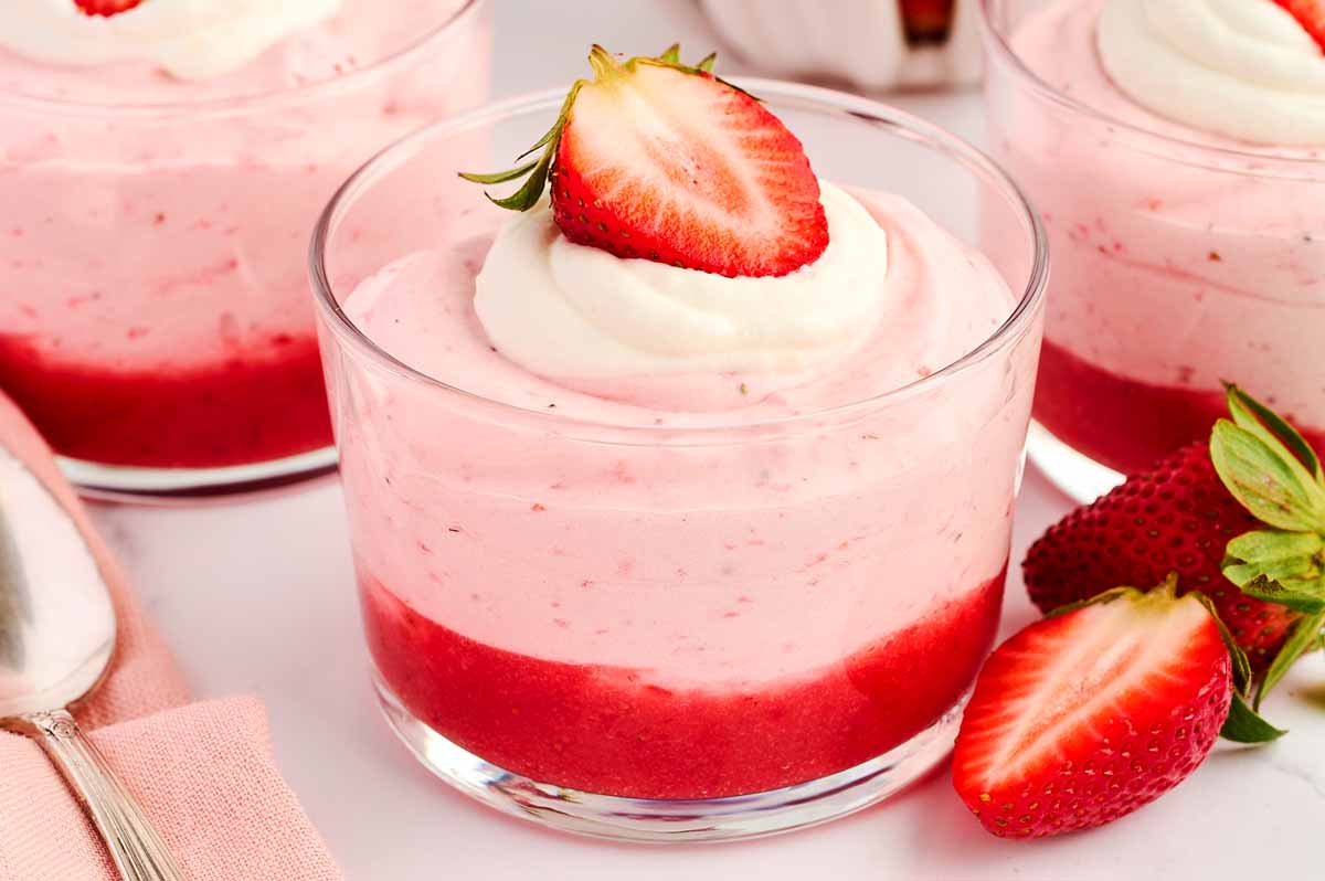 Glass cup filled with strawberry mousse, garnished with fresh strawberry.