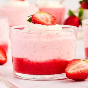 Glass cup with strawberry mousse, garnished with fresh strawberries.