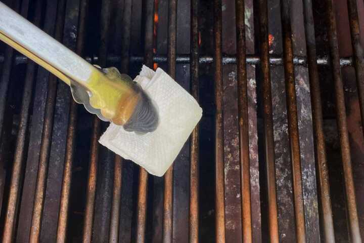 Rubbing oil on grill grates with tongs and paper towels.