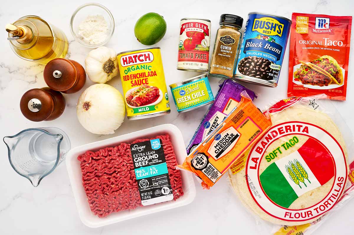 Ingredients for ground beef enchiladas on a white marble surface.