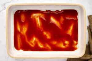 Casserole dish with enchilada sauce spread across.