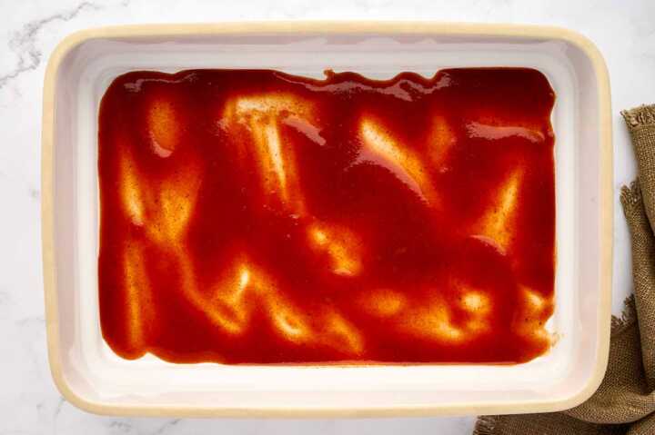Casserole dish with enchilada sauce spread across.