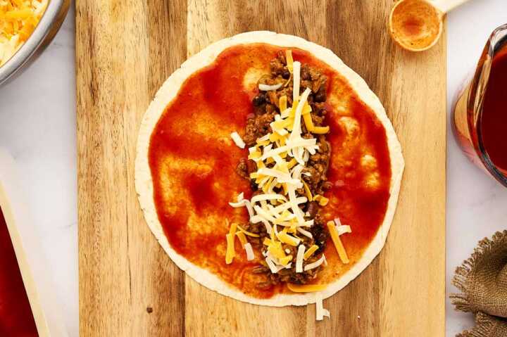 Filling enchiladas with ground beef filling and cheese.