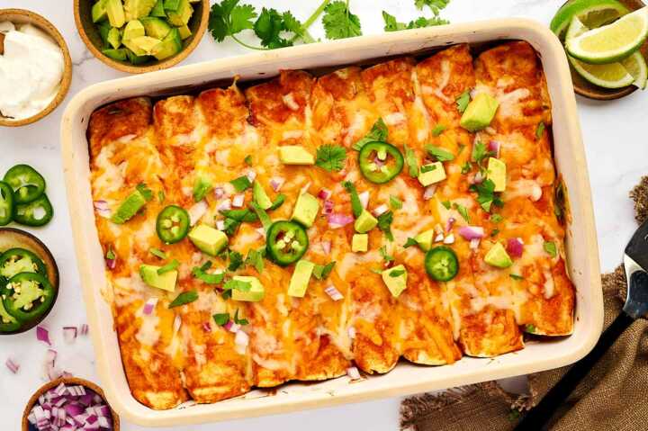Serving ground beef enchiladas in the casserole dish with toppings.