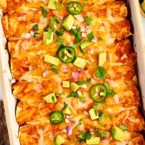 Ground Beef Enchiladas in a white casserole dish with avocado and jalapeño.