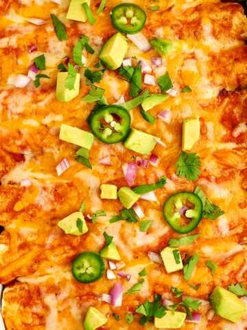 Ground Beef Enchiladas in a white casserole dish with avocado and jalapeño.