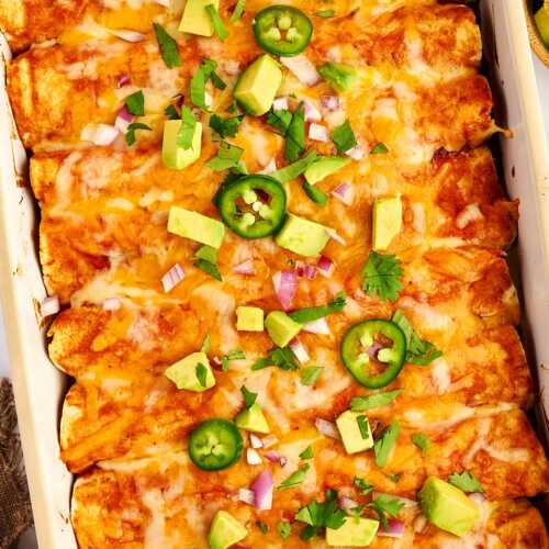 Ground Beef Enchiladas in a white casserole dish with avocado and jalapeño.