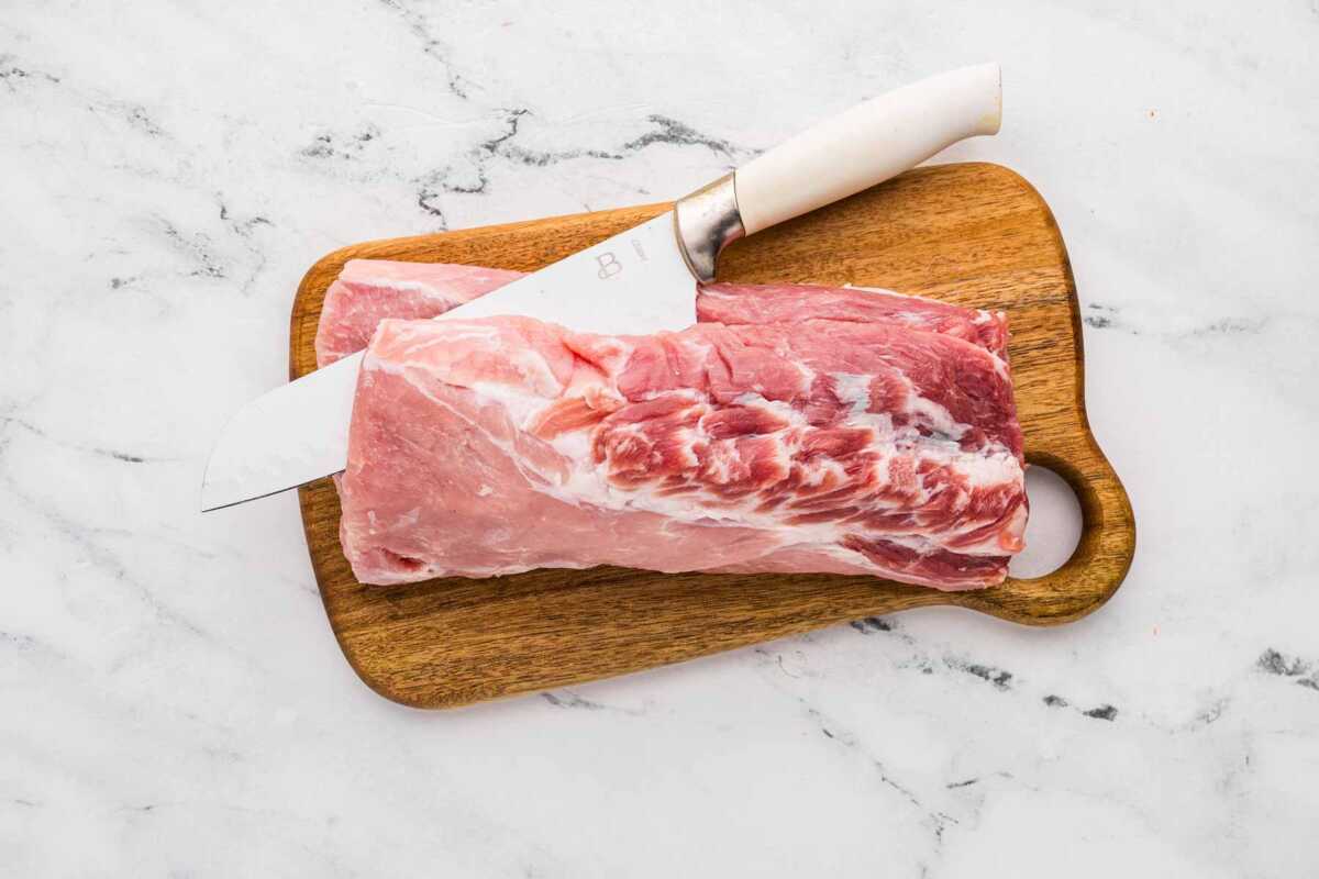 Overhead shot of a raw pork loin on a wooden cutting board with a knife.