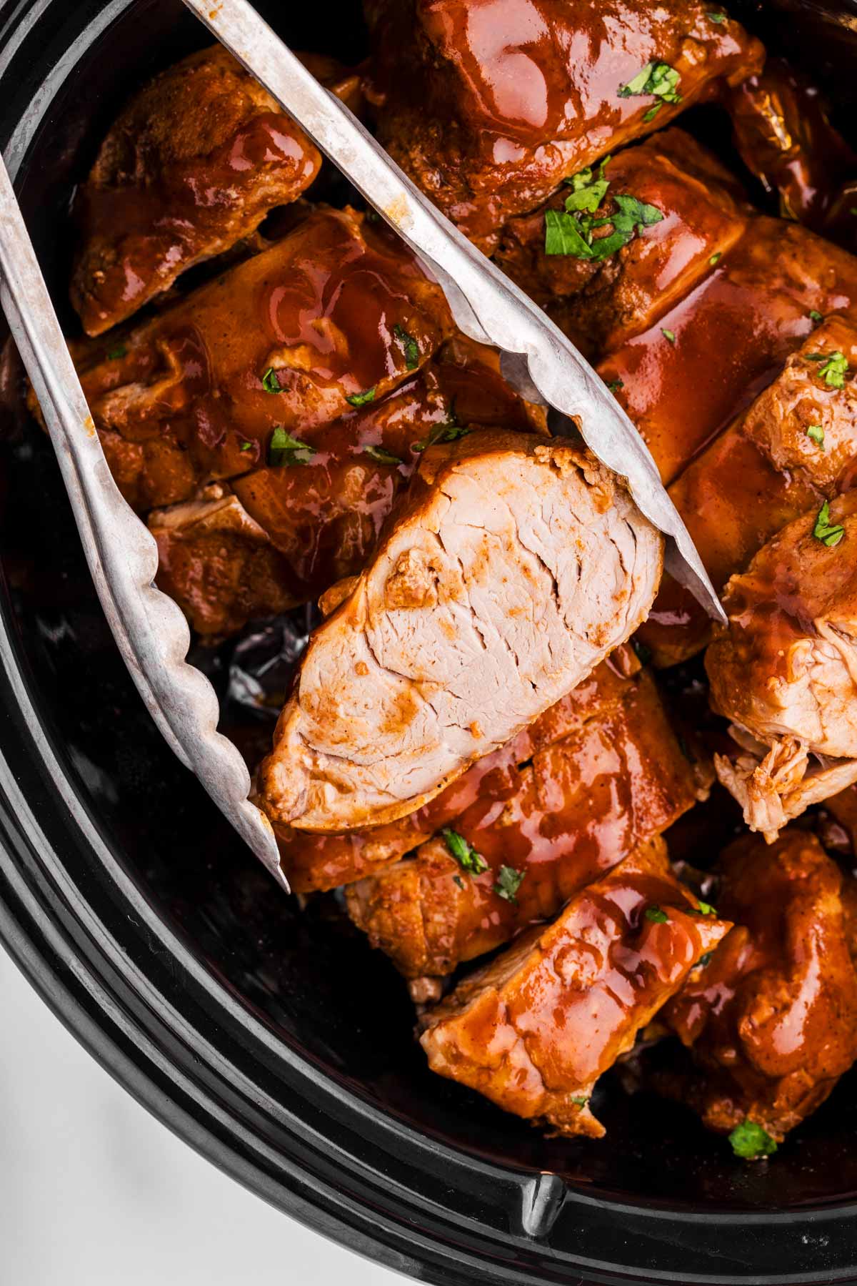 Tongs holding a slice of slow cooker pork tenderloin.