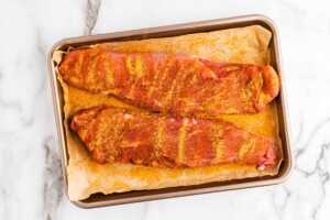 Overhead view of two raw, seasoned pork tenderloins on a lined baking sheet.