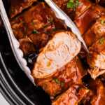 Tongs holding a slice of slow cooker pork tenderloin.