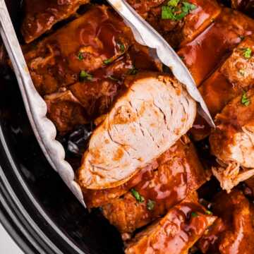Tongs holding a slice of slow cooker pork tenderloin.