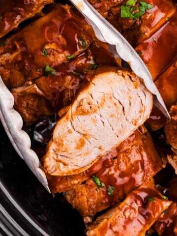 Tongs holding a slice of slow cooker pork tenderloin.
