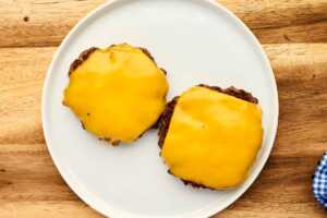 Two burger patties with cheese on a plate.