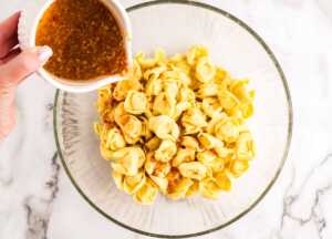 Pouring dressing over tortellini.