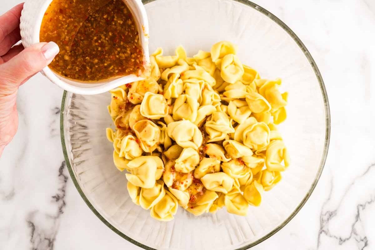 Pouring dressing over tortellini.