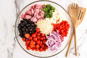Ingredients for tortellini salad in a glass bowl.