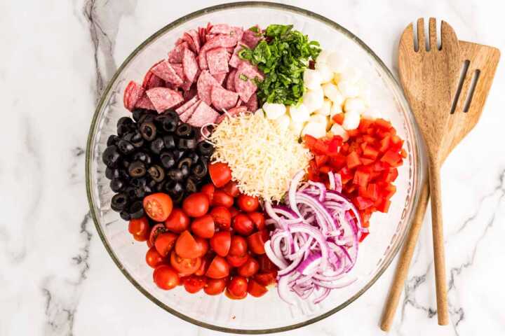 Ingredients for tortellini salad in a glass bowl.