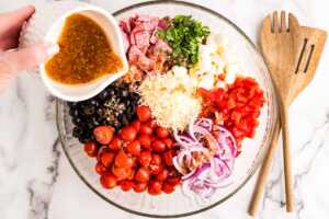 Adding dressing to bowl with ingredients for Tortellini Pasta Salad.