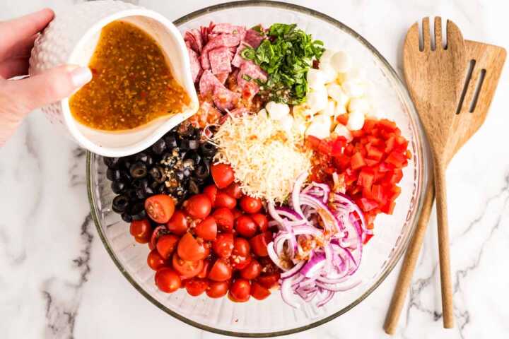 Adding dressing to bowl with ingredients for Tortellini Pasta Salad.
