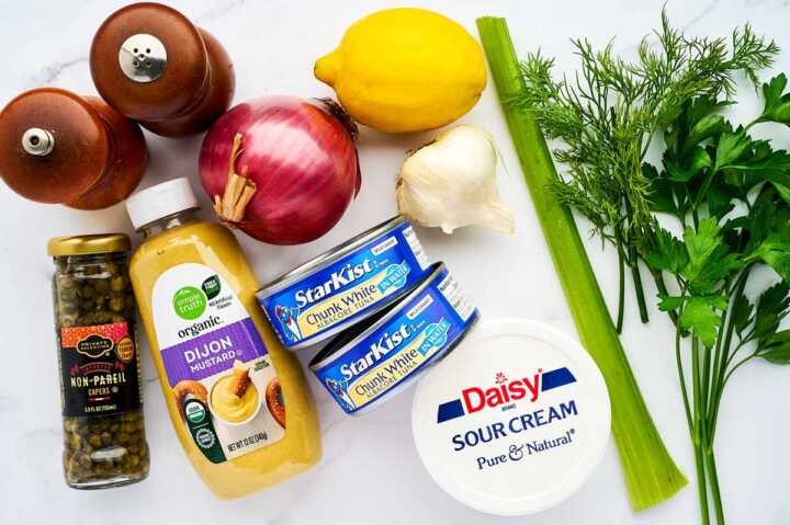 Ingredients for tuna salad on a white marble surface.