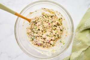 Tuna salad stirred in a glass bowl.