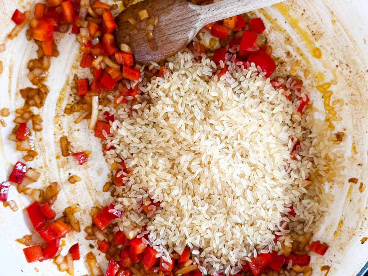 Stirring rice into vegetables in a skillet.