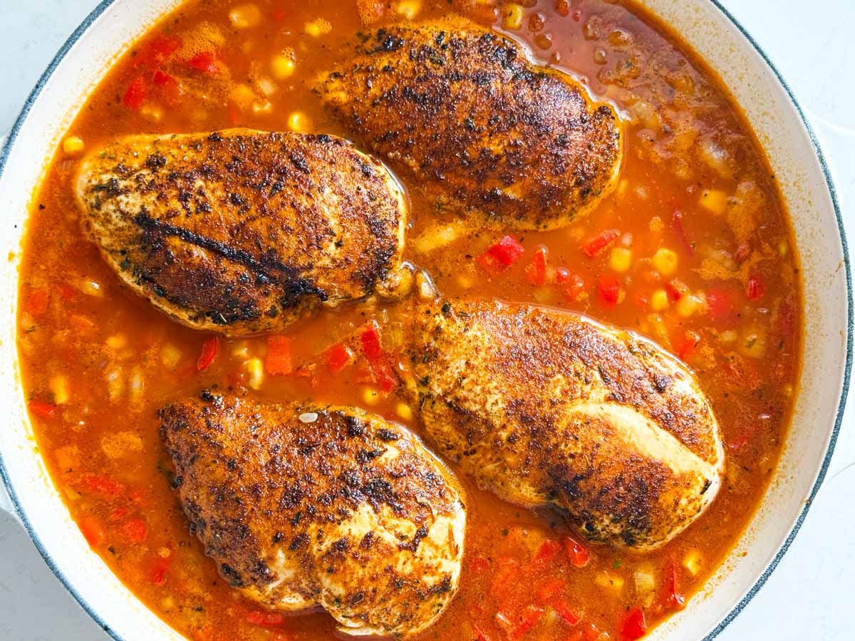 Skillet bubbling with broth, salsa, corn, and chicken.