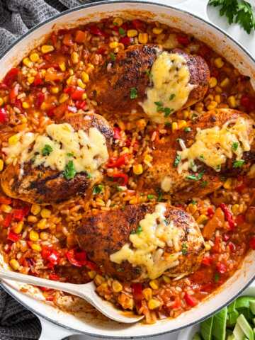 Overhead view of white skillet with one-pan salsa chicken and rice topped with melted cheese and fresh cilantro.