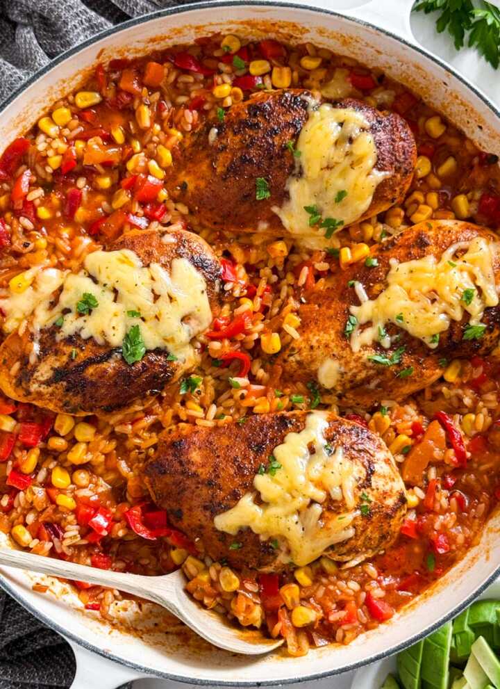 Overhead view of white skillet with one-pan salsa chicken and rice topped with melted cheese and fresh cilantro.