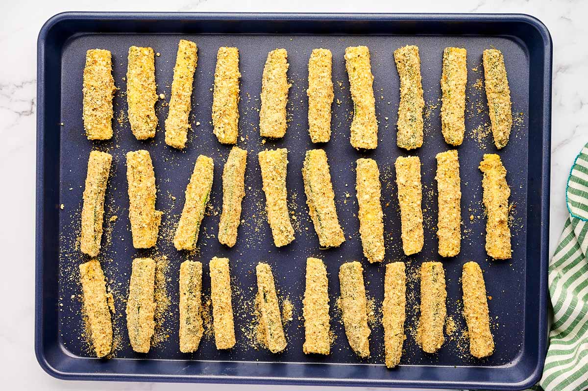 Unbaked zucchini fries on a sheet pan.