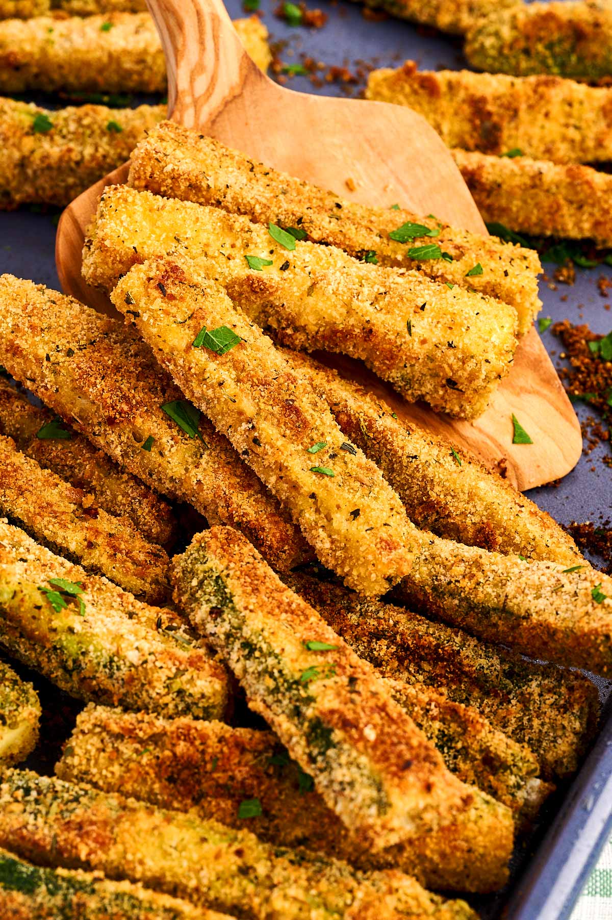 Frontal view of piled parmesan zucchini fries on a baking sheet.