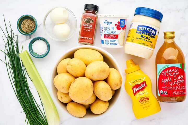 Ingredients for creamy potato salad on a white marble surface.