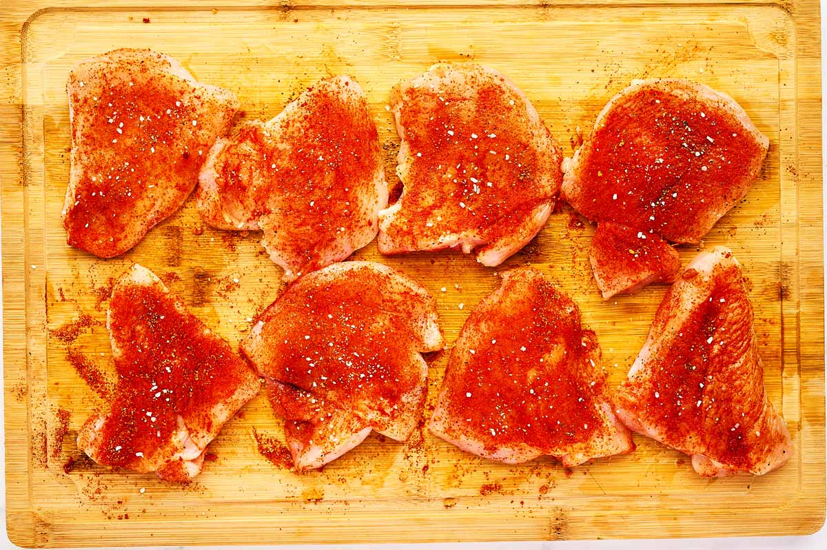 Seasoned chicken breast pieces on a wooden cutting board.