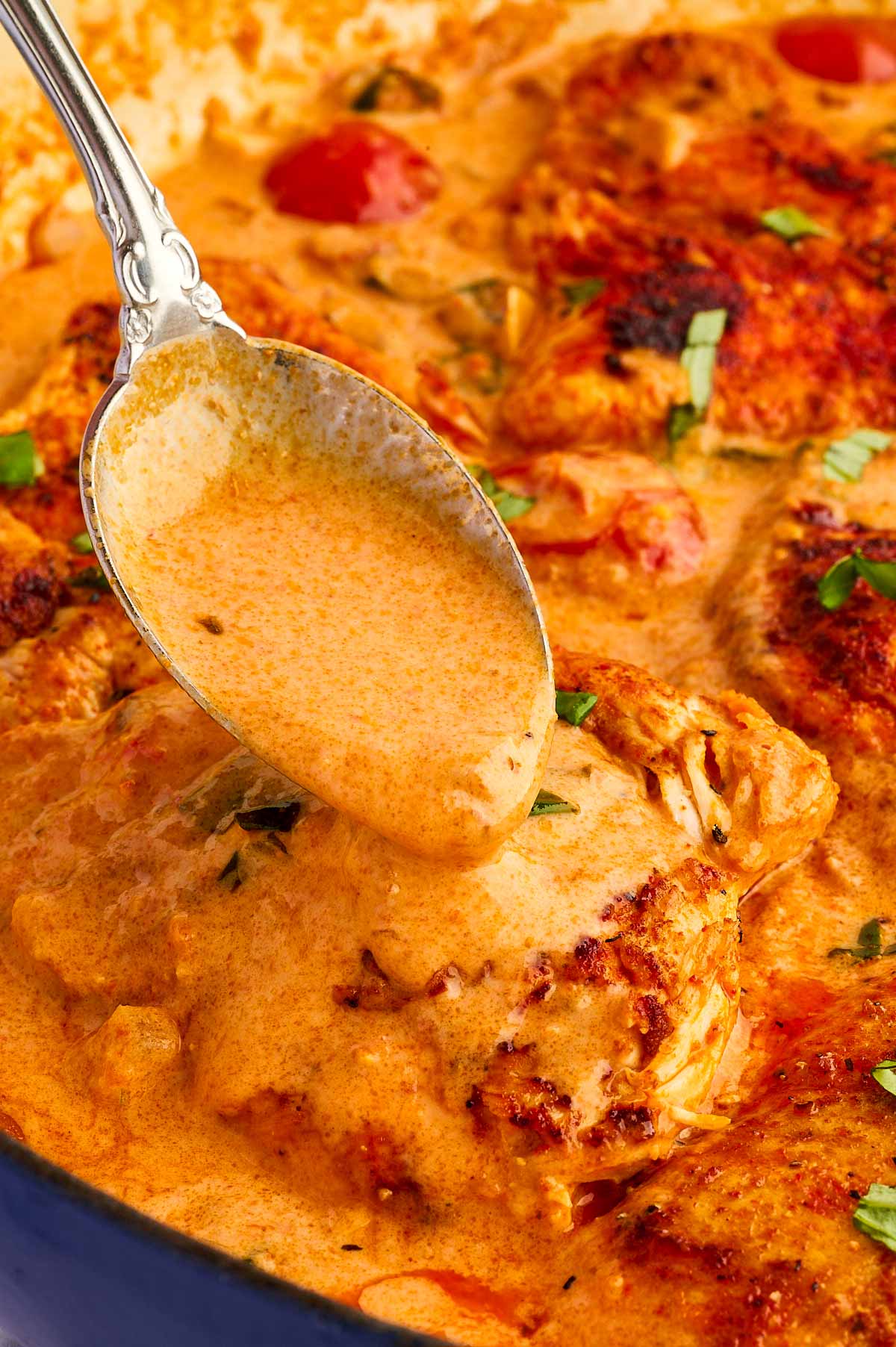 Spooning creamy tomato basil sauce over chicken.